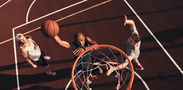 L'image montre un moment dynamique d'un match de basket-ball, où un joueur effectue un dunk puissant tandis que ses adversaires tentent de l'arrêter. Le cadre transmet la tension du jeu, la vitesse, les émotions et le véritable dynamisme du basket-ball de rue.